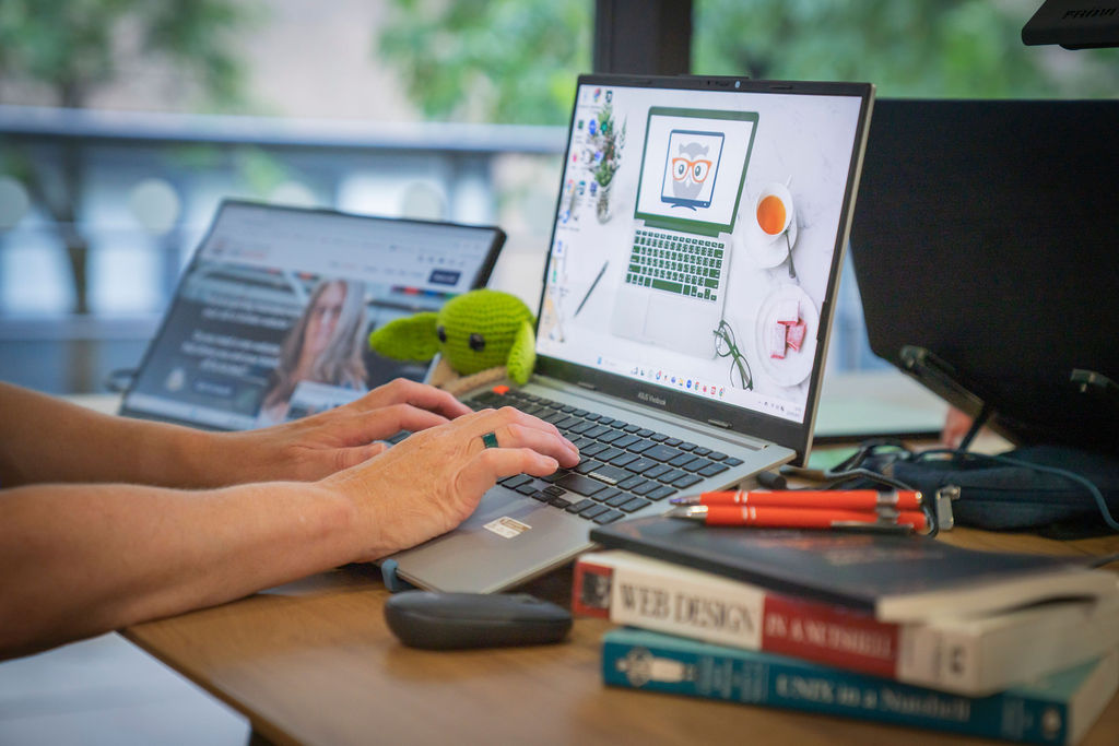 Sarah Wood small bsuiness websupport on her laptop with a crocheted grogo and 2 books